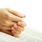 hands clasped in prayer over a Bible